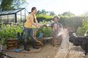 Meisje met gele shirt spuit met tuinslang man en hond in tuin