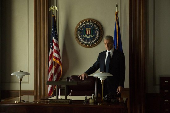 Een man in een pak staat bij een bureau met de Amerikaanse vlag en het FBI-zegel.
