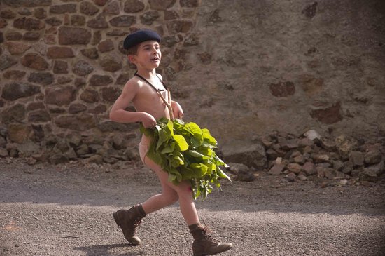 Jongetje met baret, blootsvoets, met een bos groen, loopt op straat.