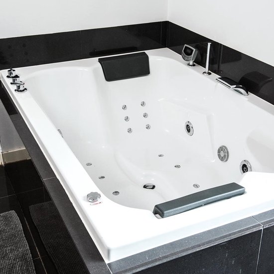 Grote witte whirlpool badkuip met zwarte hoofdsteunen, zilveren kranen en veel jets.