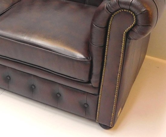 Close-up van een bruine Chesterfield fauteuil, met details van knopen en spijkers.