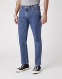 Man in een blauwe Wrangler jeans, van de zijkant, met zwarte Converse sneakers.