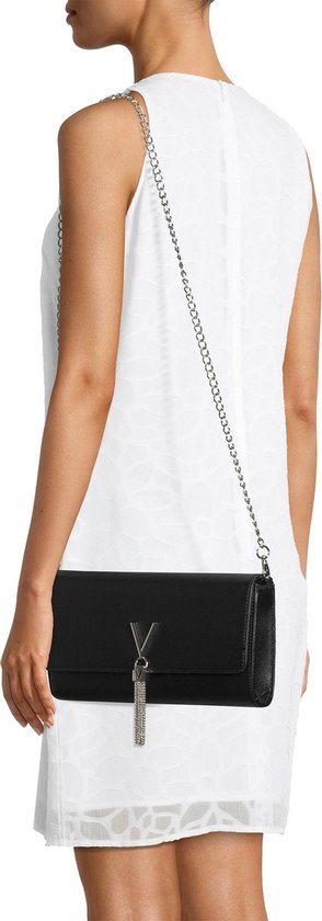Zwarte Valentino Bags clutch met zilveren V-logo en franjehanger, gedragen door een model in een witte jurk.