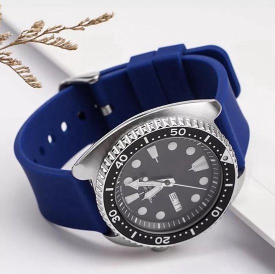 Een zilverkleurig horloge met een donkerblauwe siliconen band, gedragen op een pols.