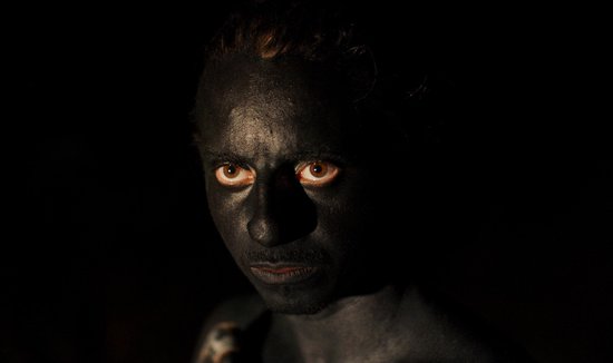 Close-up van een gezicht bedekt met zwarte verf, met bruine ogen die naar de kijker kijken.