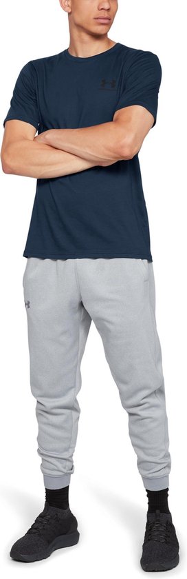 Donkerblauw sportshirt van Under Armour met zwart logo op de borst, gedragen door een man met gekruiste armen.