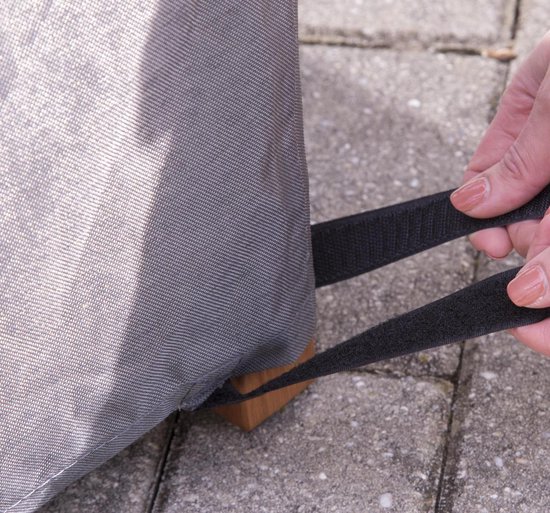 Handen sluiten de klittenbandsluiting van een grijze, ronde tuinset beschermhoes.