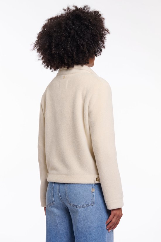 Dos de la veste courte couleur crème à col revers, avec détail de bouton doré sur la manche.