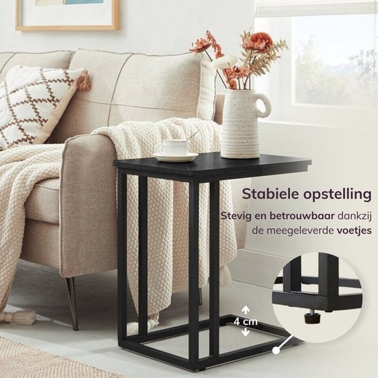 Zwart bijzettafeltje met stevige poten, 4 cm hoog, naast een bank.