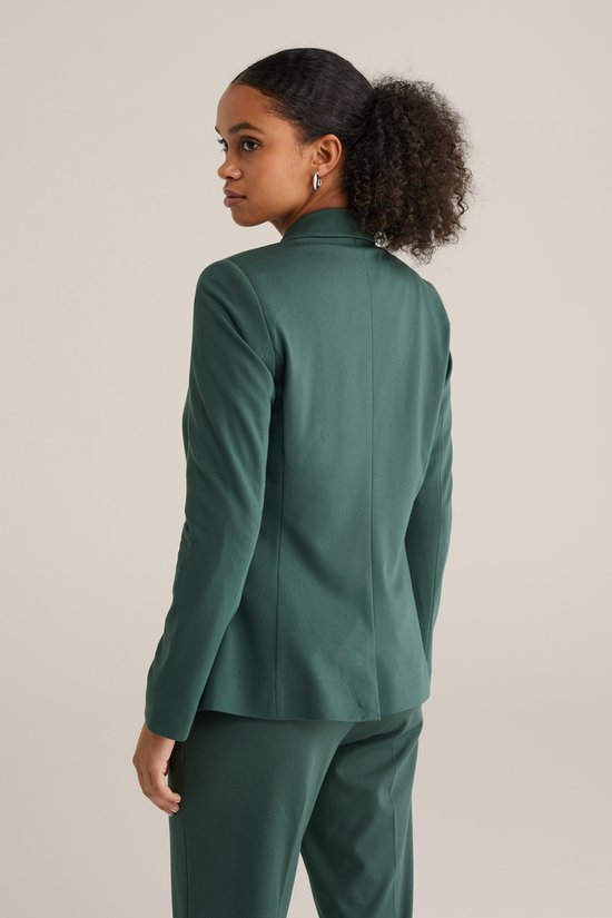 Model van achteren gezien, draagt een donkergroene blazer met broek.