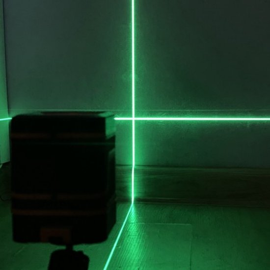 Groene laserlijnen die een kruis vormen op een muur en vloer, met een zwarte laserwaterpas.