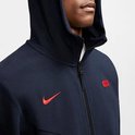 Close-up van een donkerblauw Nike Tech vest met capuchon, rode Nike logo en rood embleem.