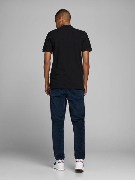 Man met rug naar camera in zwarte polo en donkere broek