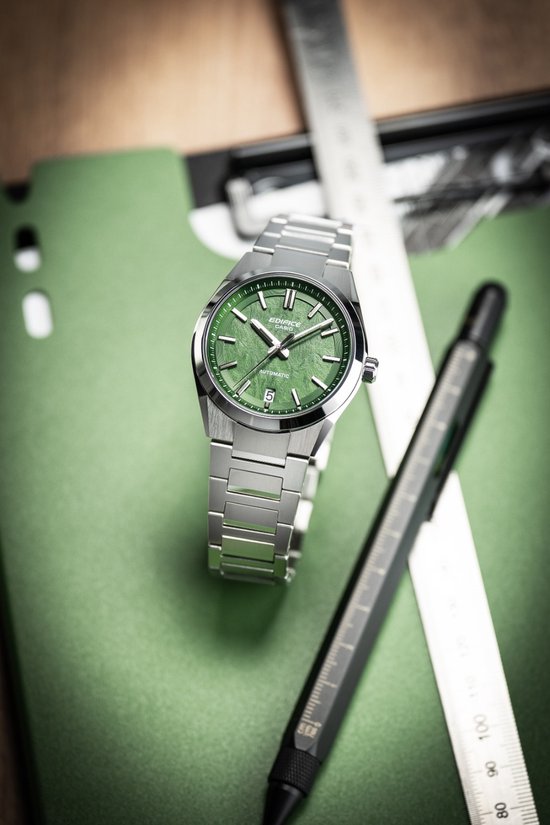 Edifice horloge met groene wijzerplaat, naast een liniaal en pen.