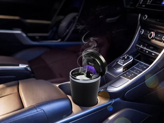 Zwarte aut asbak met zilveren rand, blauw LED licht en rook, staand in een auto console.