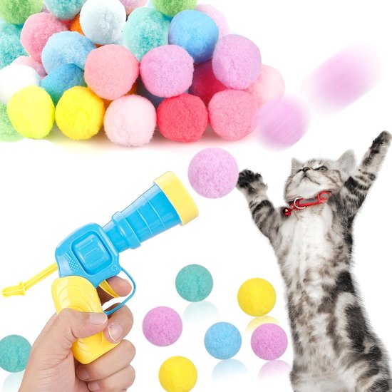 Een grijze kitten speelt met een blauw-geel speelgoedpistool dat een roze pompon lanceert. Veelkleurige pompons liggen op de grond. Tekst "PLUSH FUZZY BALLS".