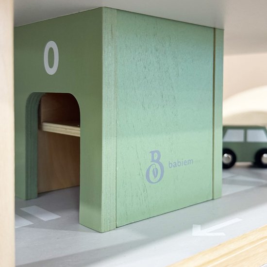 Close-up van pastelgroen houten speelgoedgarage-onderdeel met '0' en Babiem logo, met een deel van een groene auto.
