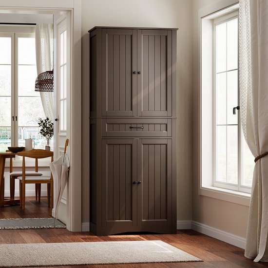 Haute armoire de cuisine marron foncé avec portes et tiroir fermés, placée dans un salon à côté d'une fenêtre et d'un coin repas.