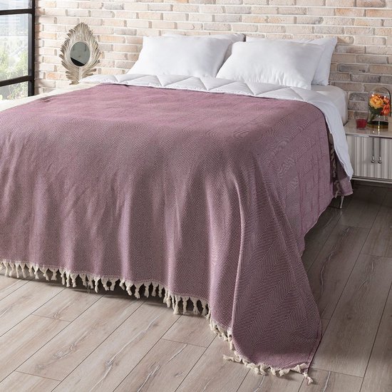 Bourgondische sprei met visgraatpatroon en crème witte franjes, gedrapeerd over een bed.