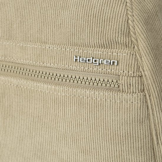 Close-up van het Hedgren logo op een beige ribfluwelen rugzak met ritssluiting.