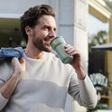 Homme buvant d'une tasse vert clair dans ses mains à l'extérieur.
