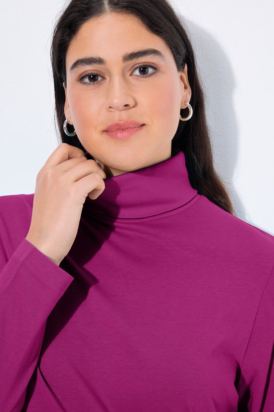 Close-up van een model in een fuchsia coltrui, terwijl ze haar kraag aanraakt.