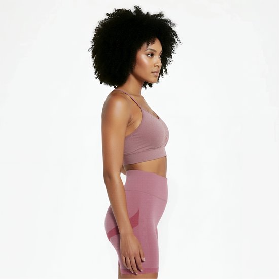 Vrouw met afro haar, van de zijkant gezien, draagt een roze sportbeha en fietsbroek.