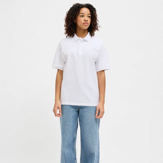 Vrouw met krullend haar, draagt een wit poloshirt en denim jeans.