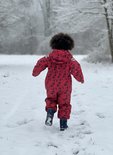 Meisje in rood regenpak met donkerblauwe bloemenprint, wegrennend in de sneeuw.