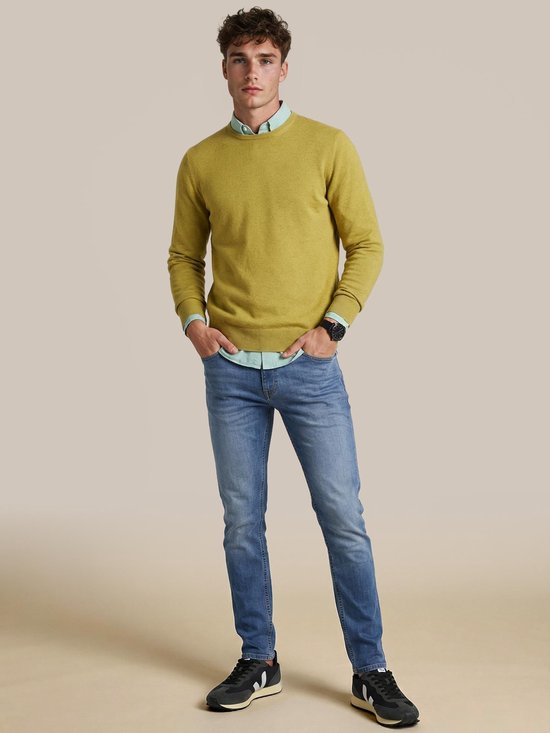 Homme debout portant un pull Steppin' Out vert mousse sur une chemise vert pâle, un jean bleu et des baskets.