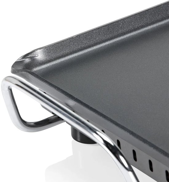 Detail van de hoek van een zwarte elektrische bakplaat met metalen handvat.