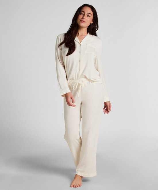Model in een crèmewitte pyjamaset met lange mouwen en knoopsluiting.