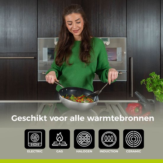 Een vrouw met een groene trui kookt in een wokpan met een zilveren handvat. De pan is geschikt voor alle warmtebronnen.