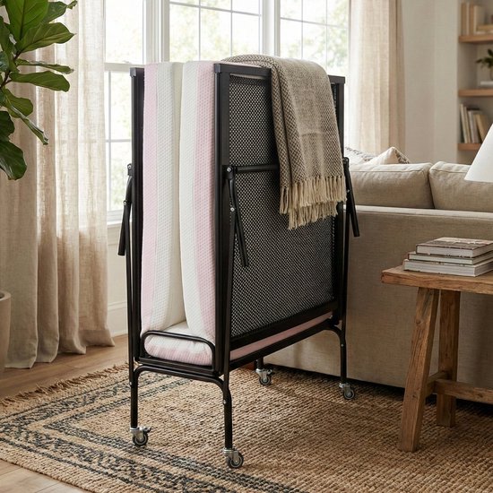 Zwart opklapbed met opgerolde witte en roze matrassen en een beige plaid.