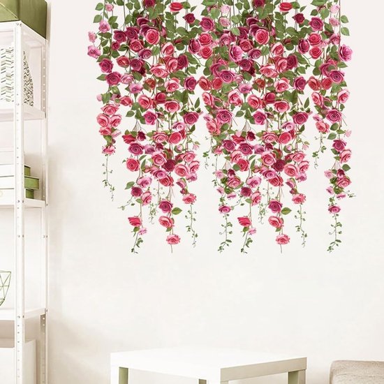 Hangende roze en rode rozen met groene bladeren op een witte muur naast een witte boekenkast.