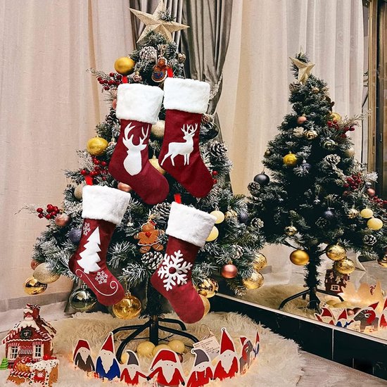Quatre bas de Noël rouges à bords blancs et motifs de Noël: cerf, arbre et flocon de neige. Suspendus à un petit sapin de Noël.