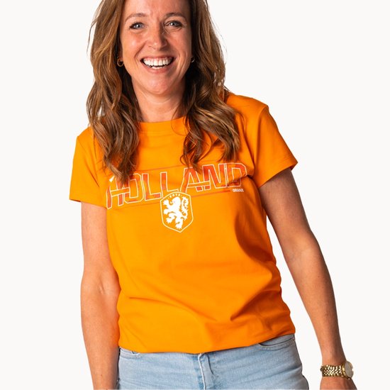 Femme souriante portant un t-shirt orange HOLLAND avec logo lion. Jean avec bracelets dorés et montre.