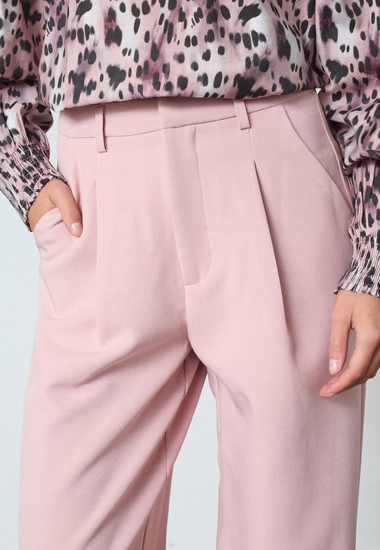 Detail van een lichtroze wijde broek met plooien aan de voorkant.