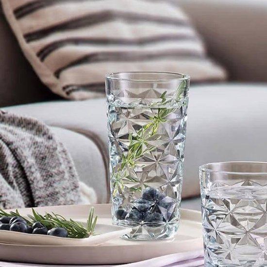 Een hoog, geribbeld glas gevuld met water, munt en bosbessen staat op een dienblad. Een ander glas en een bakje met munt en bosbessen staan ernaast.