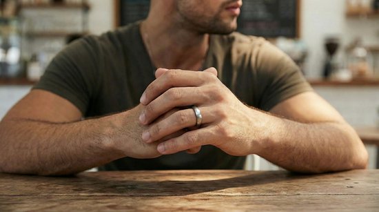 Man zit aan tafel met de armen gekruist, draagt een matte zilverkleurige wolfraamring om de ringvinger.