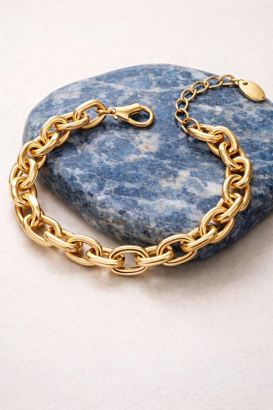 Gouden schakelarmband met grove schakels, liggend op een blauwe steen.