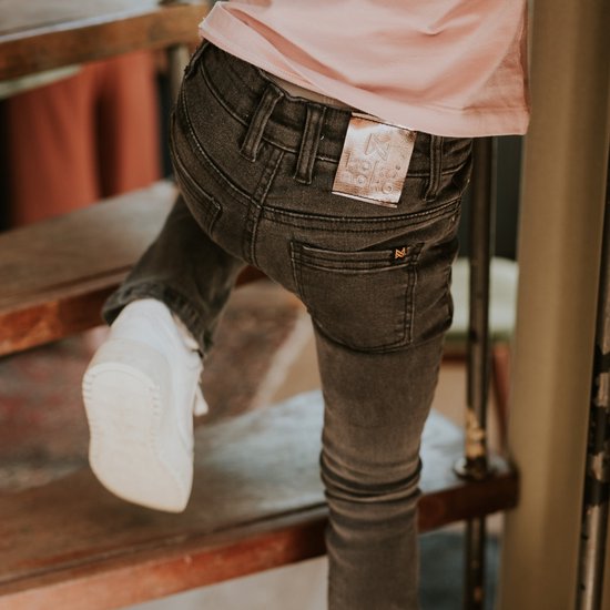 Meisje in donkergrijze jeans met roze shirt, lopend op een trap.
