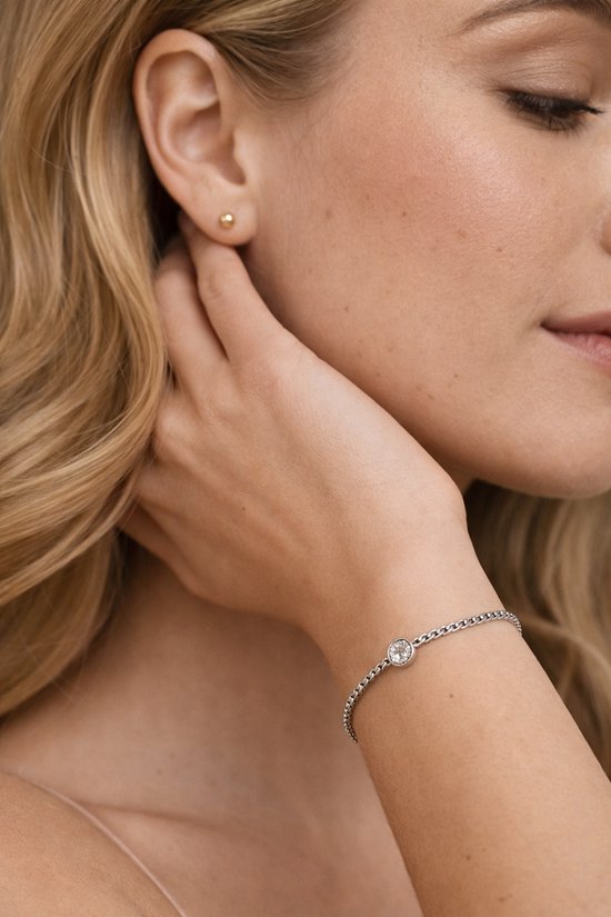 Model draagt een zilverkleurige armband met een enkele zirkonia, bijpassend bij haar oorbel.