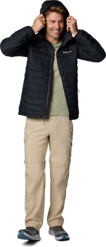 Man in zwarte Columbia jas en beige cargobroek, zet capuchon op.