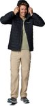 Man in zwarte Columbia jas en beige cargobroek, zet capuchon op.