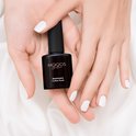 Houdt een flesje 'Americano Coffee Nude' nagellak vast. De nagels zijn wit gelakt.