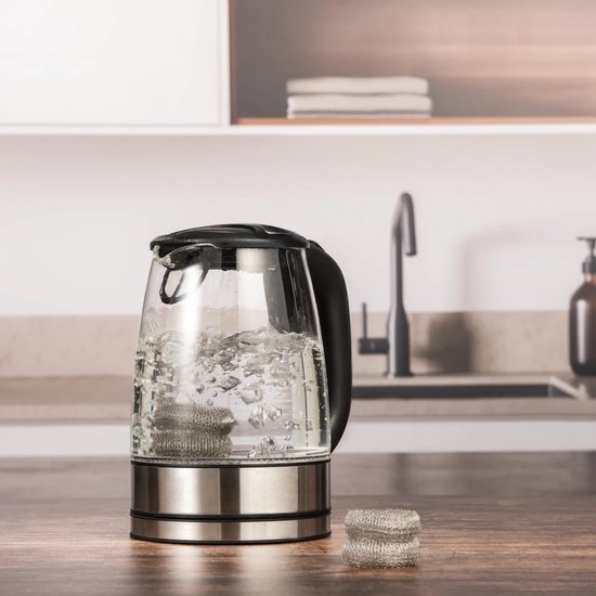 Een glazen waterkoker met kokend water, waarin twee metalen kalkvangers liggen. Naast de waterkoker ligt een stapel van twee kalkvangers.