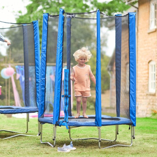 Jongetje met blond haar staat springend op een blauwe Plum trampoline in de tuin.