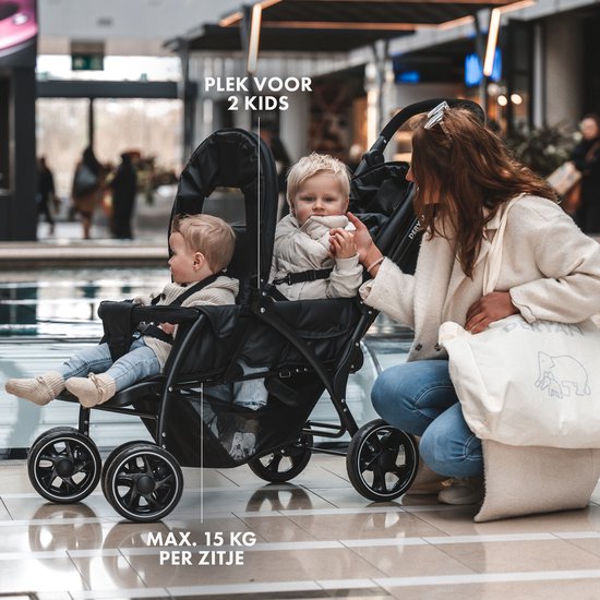 Zwarte dubbele buggy met twee kinderen, een vrouw buigt naar de kinderen.
