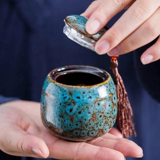 Handen die een kleine blauwe keramische urn met deksel openen.